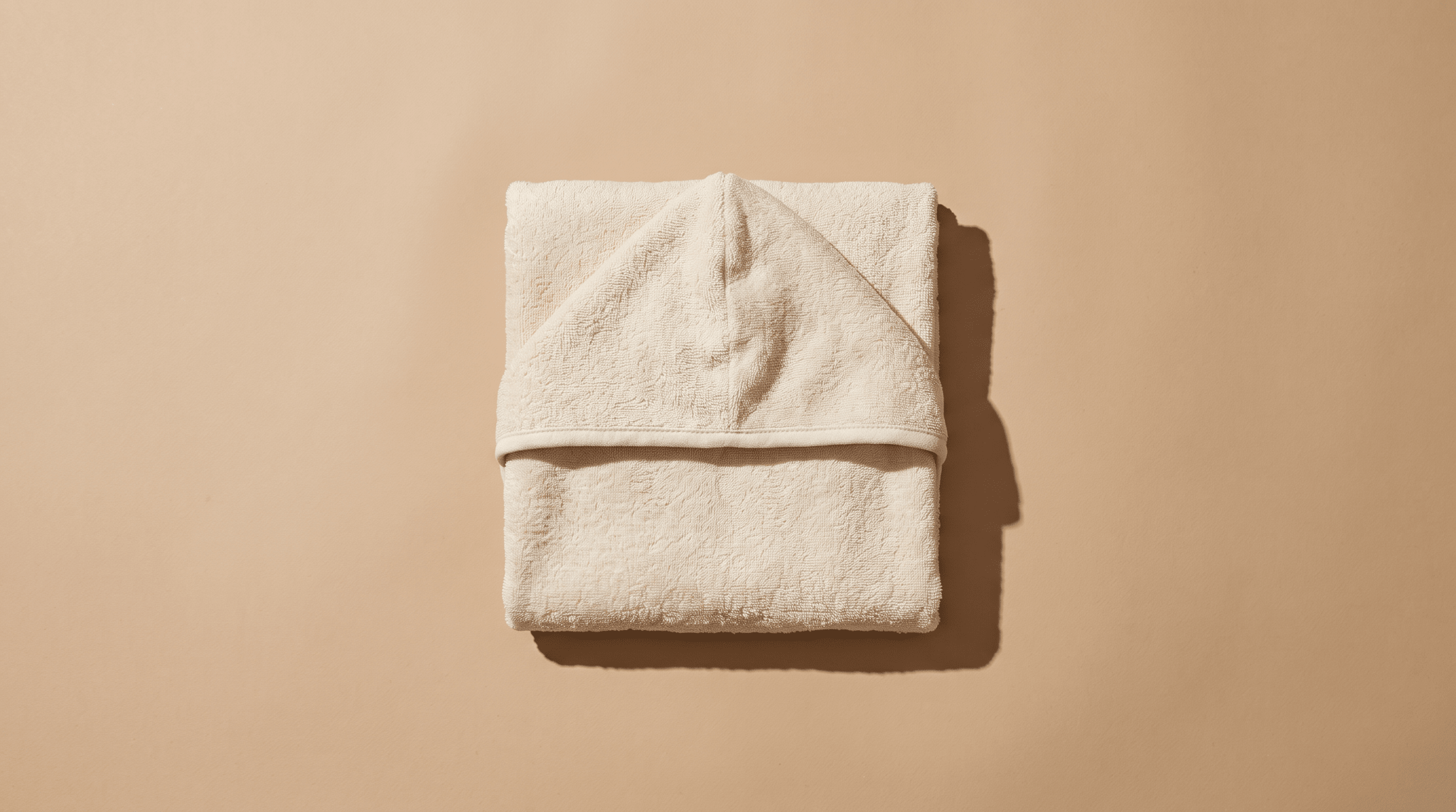 Cape de bain bébé en coton pliée sur fond neutre — guide Treelys®